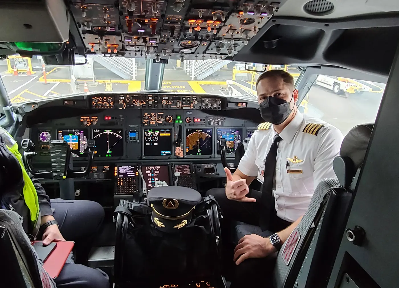An airline pilot giving a shaka beside a cat carrier in the cockpit