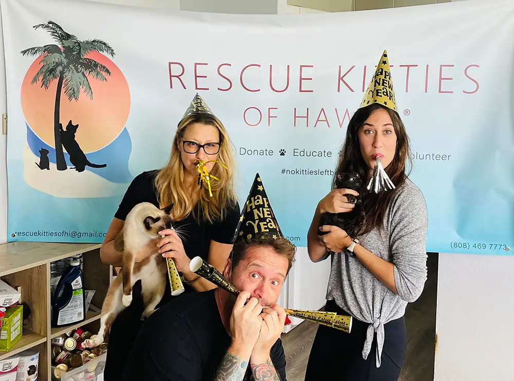 Volunteers in party hats holding cats in front of the rescue banner