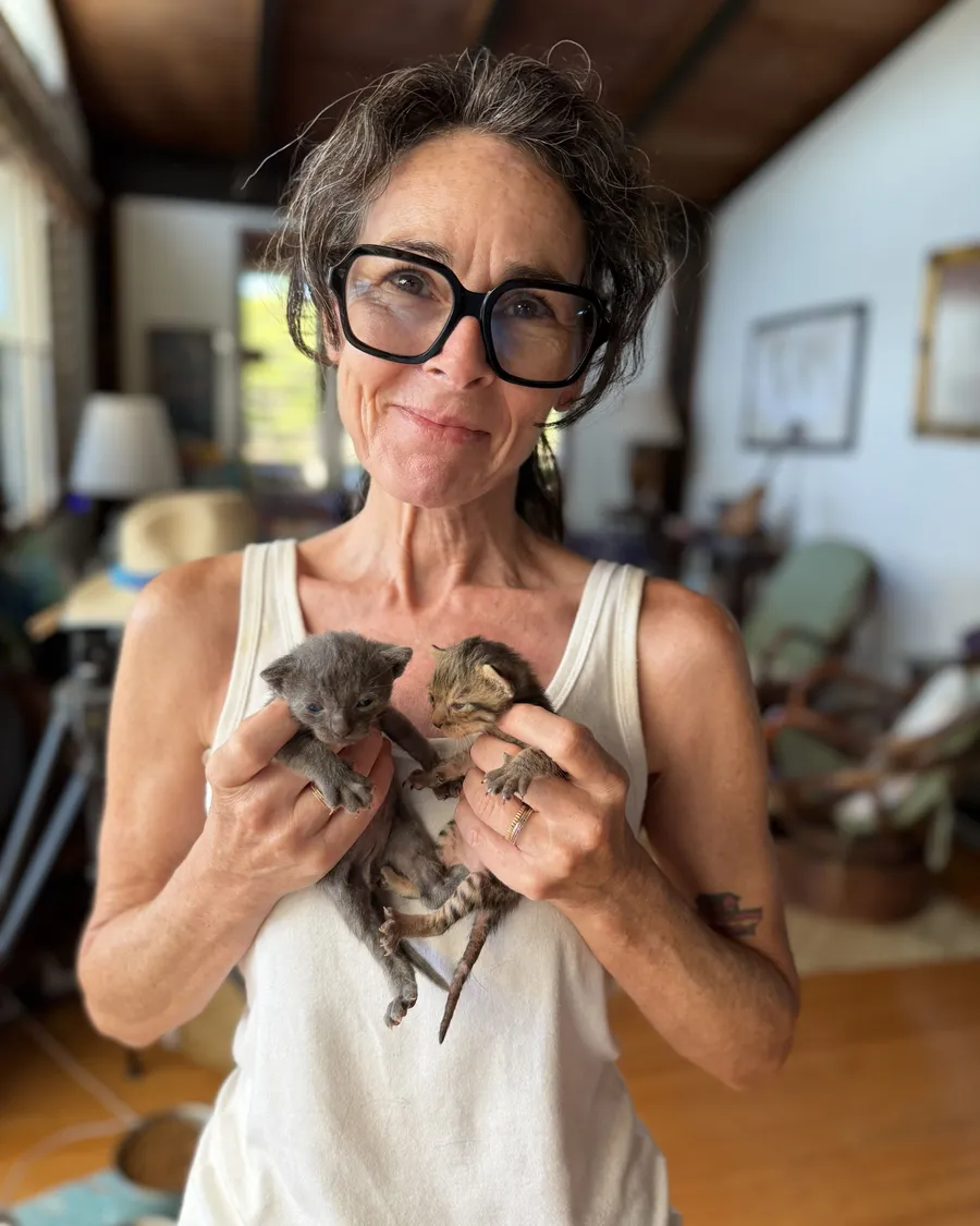 A smiling volunteer holding two newborn kittens